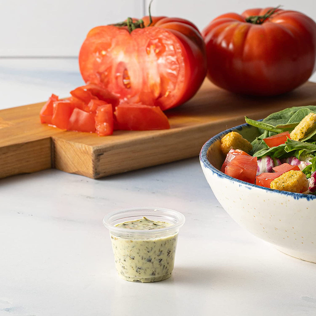 1oz Clear Sauce Cup source up on a table with tomato and salad