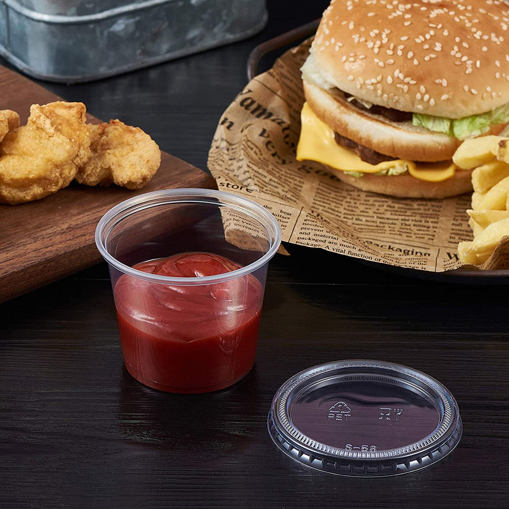 5.5oz Clear Sauce Cup with tomato sauce and chicken nugget sitting next to it